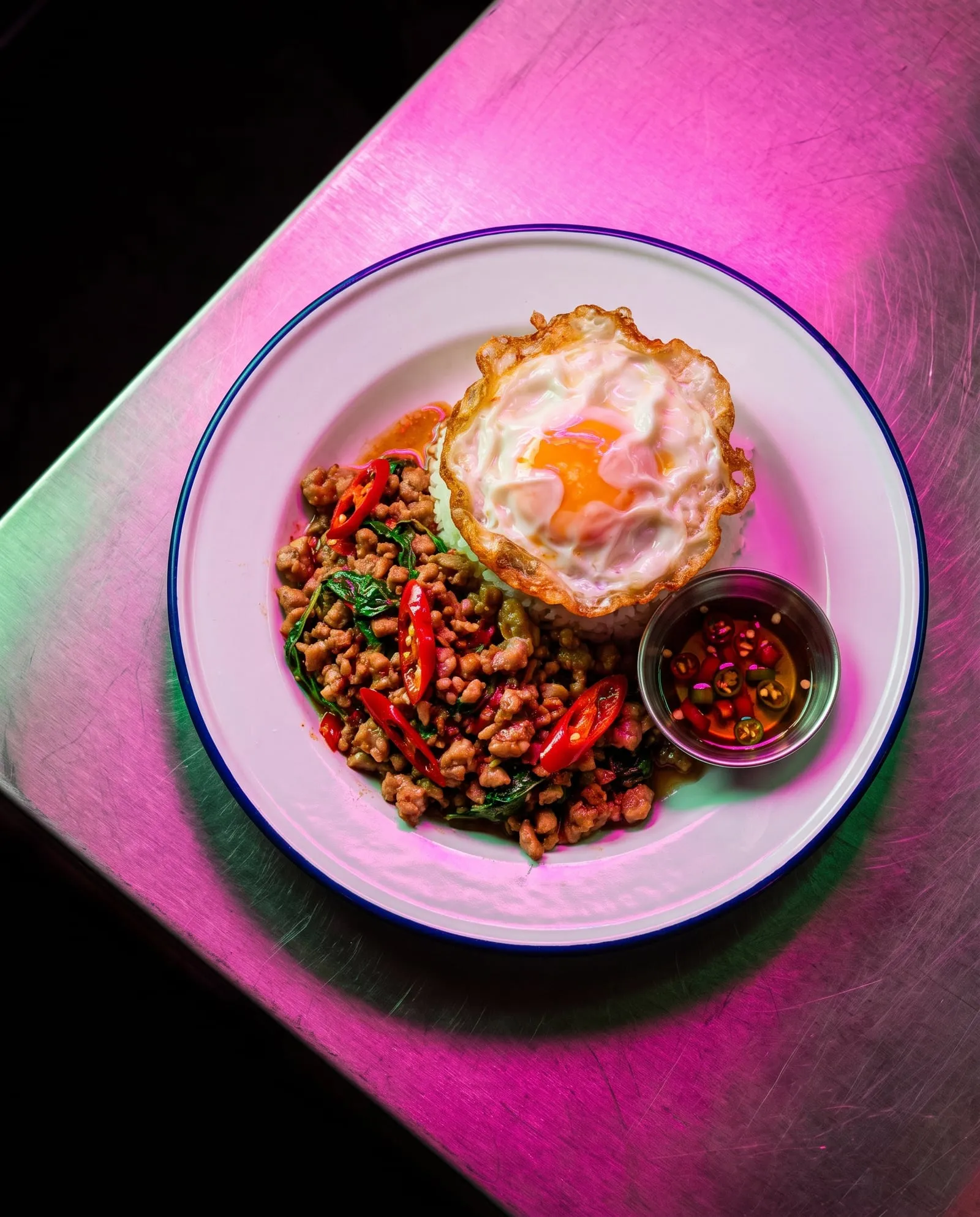 Holy basil stir-fry with chilli and a crispy fried egg on rice, on a steel table