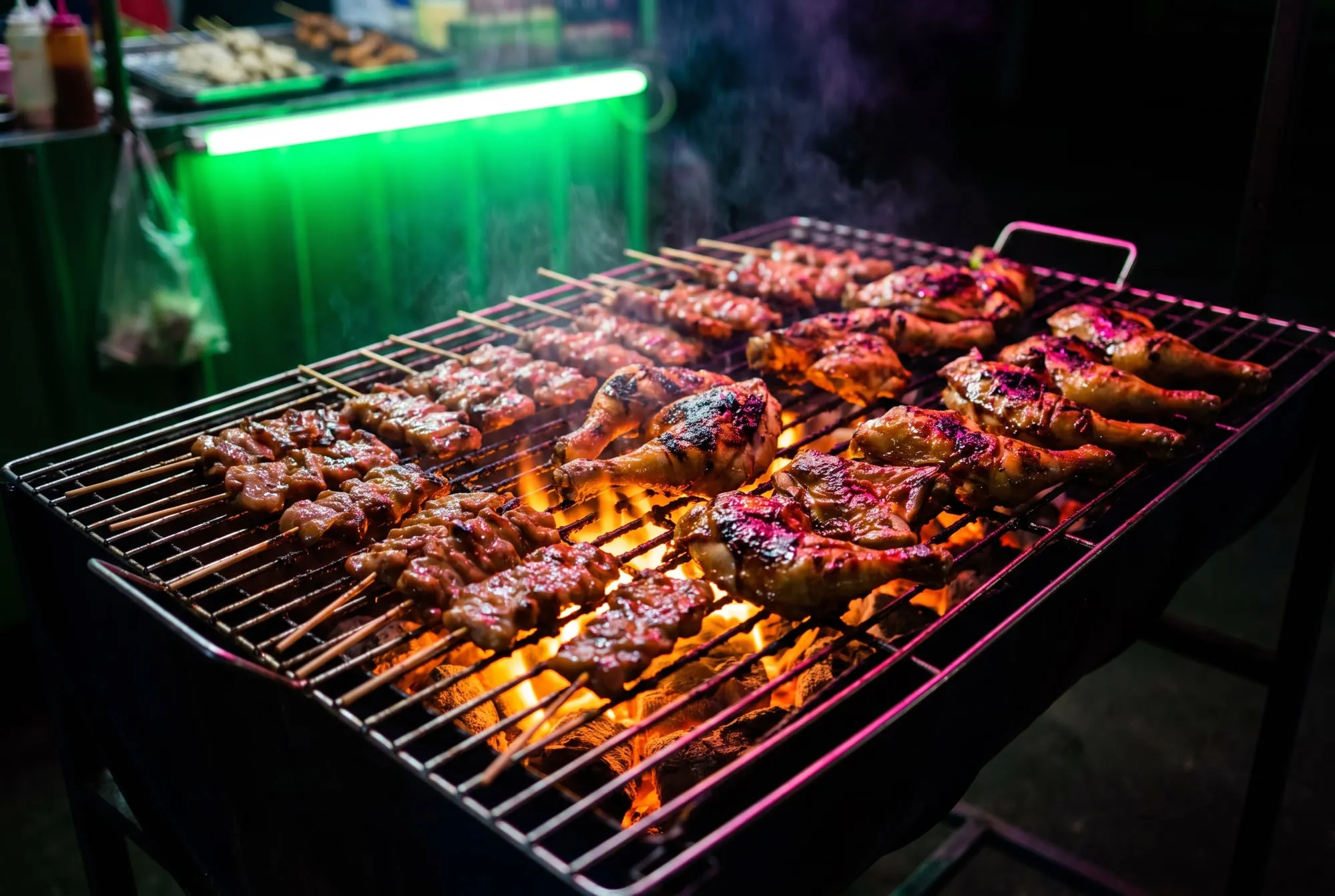 Pork skewers and chicken charring on a charcoal grill with smoke rising
