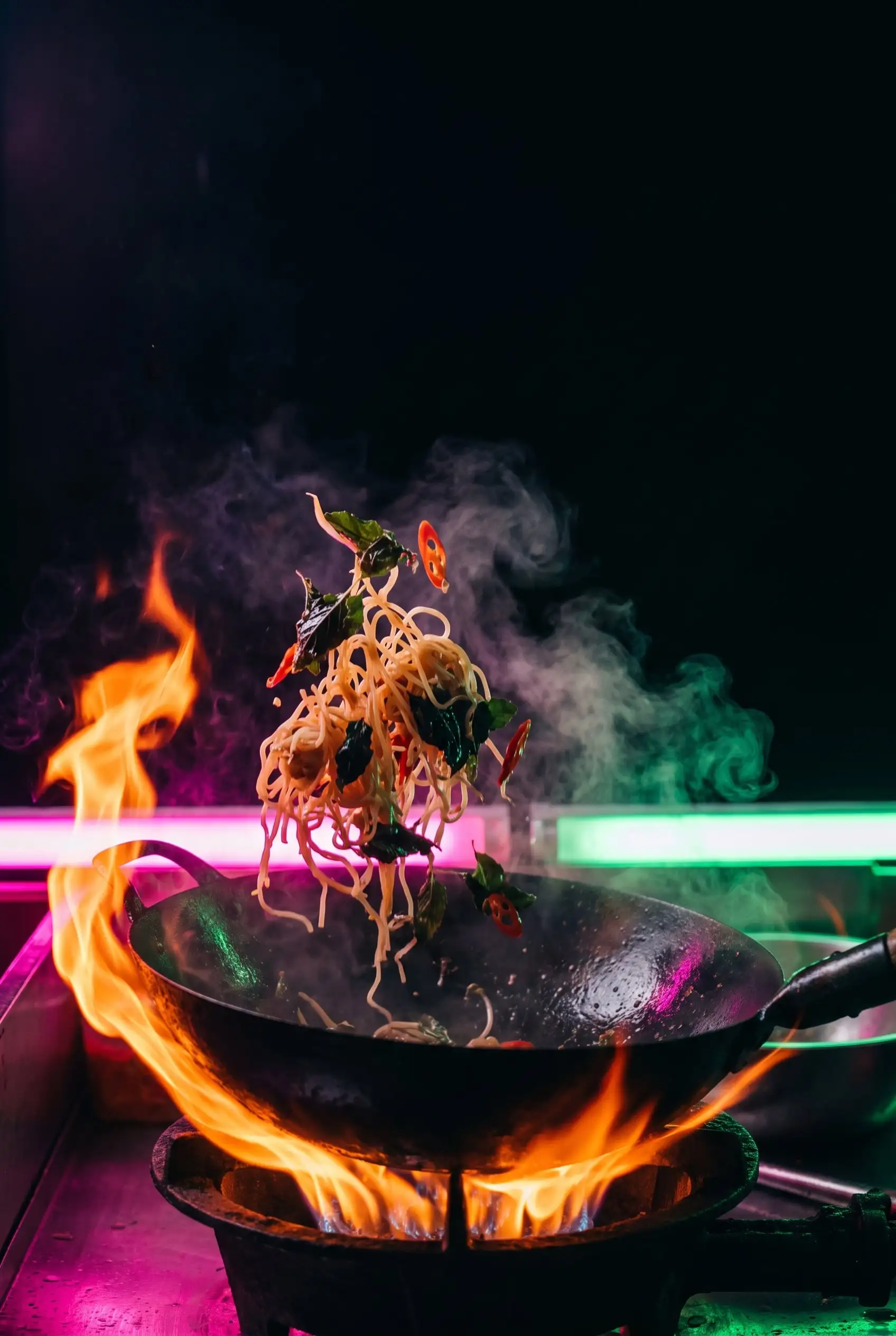 Noodles, basil and chilli tossed above a wok wrapped in orange flame